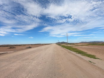 Dirt road by land against sky