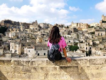 Rear view of woman sitting on retaining wall in city