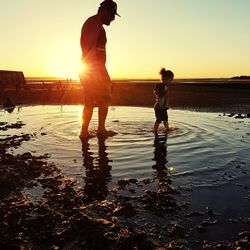 Men standing on beach against sky during sunset