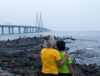 Rear view of people standing on rock by sea against clear sky