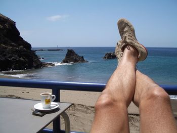 Low section of person relaxing on sea against sky