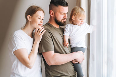 Happy multinational family father young man and mother with baby girl near window room at home