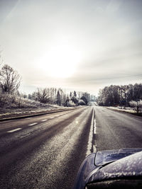 Road by trees against sky during winter