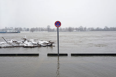 Road sign by lake against clear sky