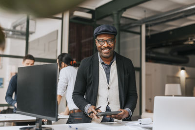 Portrait of smiling businessman with tablet pc standing at desk in office