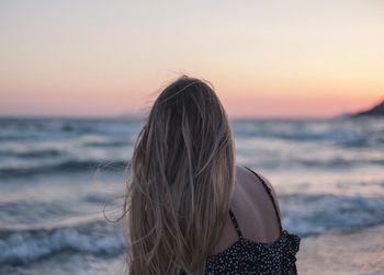 Woman looking at sea shore against sky during sunset