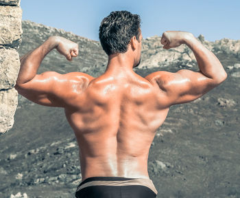 Rear view of shirtless muscular man flexing muscles on field