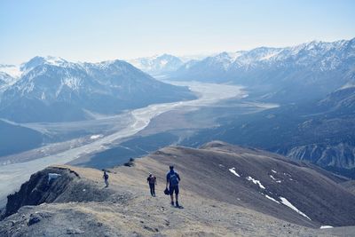 Rear view of people walking on snowcapped mountain against clear sky