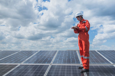 Engineer standing on solar panel against cloudy sky