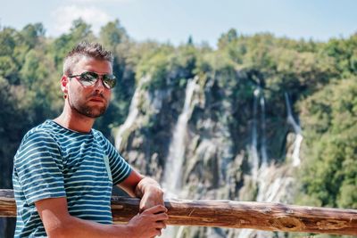 Portrait of young man wearing sunglasses standing against trees