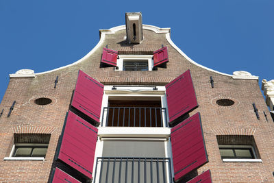 Low angle view of red shutters on a canal house in amsterdam against blue sky