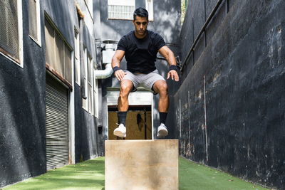 Full body of serious hispanic male in sportswear jumping on wooden box during active training