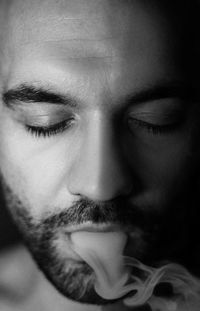 Close-up of young man with closed eyes emitting smoke