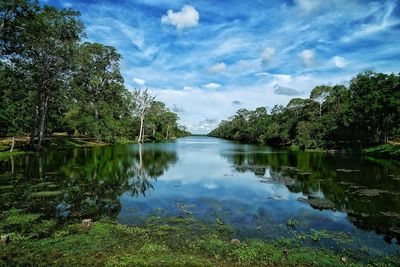 Scenic view of calm lake amidst trees against blue sky