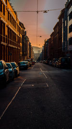 Cars on road amidst buildings in city against sky during sunset