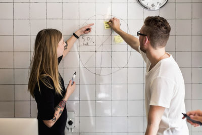 Young business people putting adhesive notes on wall in new office