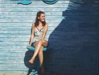 Young woman sitting on table by blue wall