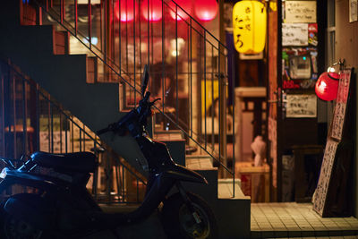 Motor scooter parked by steps outside store at night