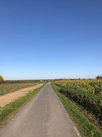 Road amidst field against clear blue sky