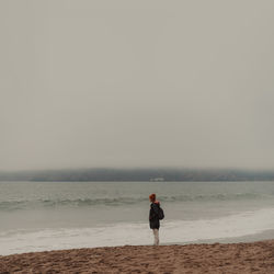 Rear view of man standing on beach against clear sky