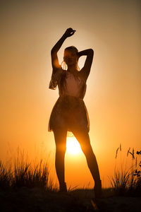 Silhouette woman standing on field against orange sky