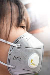 Close-up of girl wearing pollution mask against sky