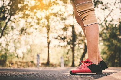 Low section of woman walking on road against trees