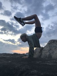 Surface level of girl doing handstand on land against sky during sunset