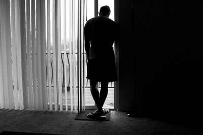 Full length rear view of silhouette man standing near window at home