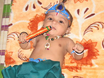 Portrait of cute baby boy in traditional clothing holding flute on bed during krishna janmashtami