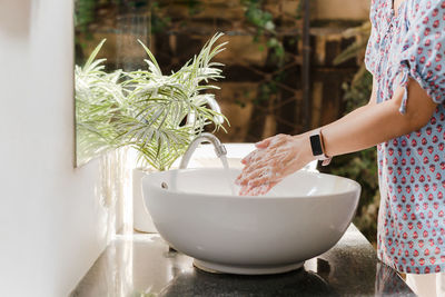 Woman washing hands with tap water under faucet at white sink