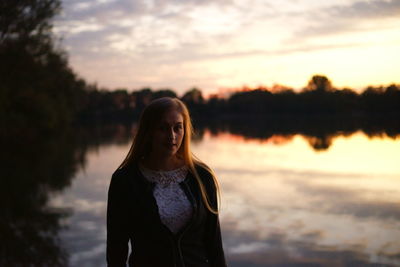 Portrait of young woman standing by lake during sunset