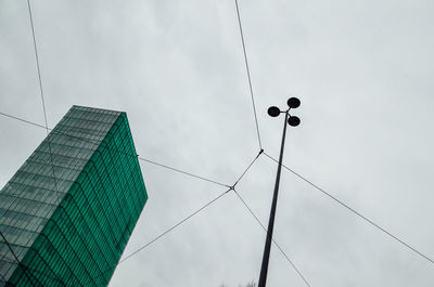 Low angle view of street light and cables with building against sky