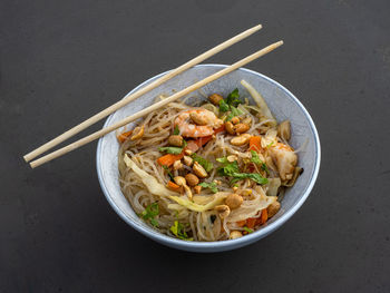Fresh shrimps, noodles, vegetables, and crunchy peanuts in an elegant white bowl with chopsticks.