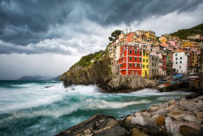 Buildings by sea against cloudy sky