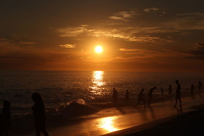 Silhouette people on beach against sky during sunset