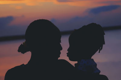 Close-up of silhouette mother with daughter at beach sky during sunset