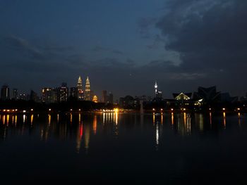 Illuminated buildings by river against sky at night