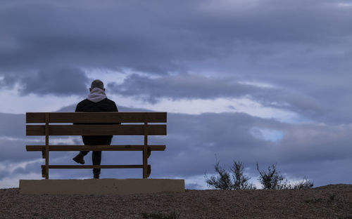 Rear view of man sitting on bench against cloudy sky. almeria, spain
