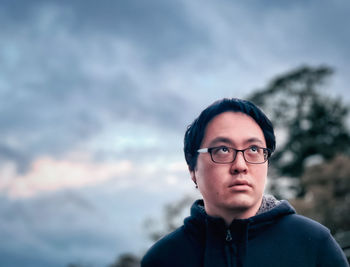 Portrait of young man in eyeglasses against cloudy sunset sky.