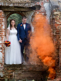 Full length of newlywed couple standing by abandoned built structure