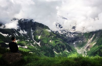 Rear view of woman sitting on mountain against sky