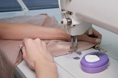 Cropped hands of woman using sewing machine