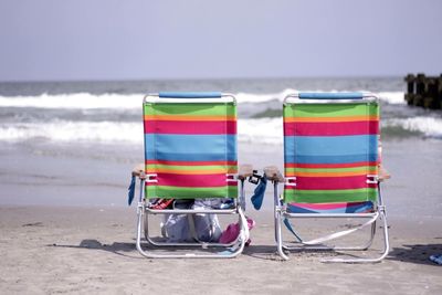 Colorful folding chairs on shore at beach against sky