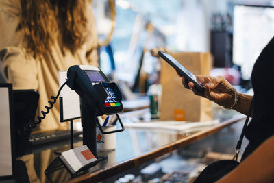 Cropped image of male customer paying through smart phone to female owner at clothing store