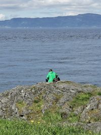 Man sitting on rock by sea against sky