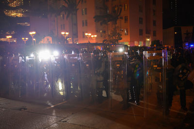 People standing on illuminated street by buildings at night