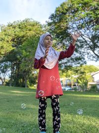 Full length of woman standing on field playing bubble