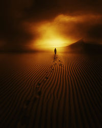 Silhouette person walking on sand against sky during sunset