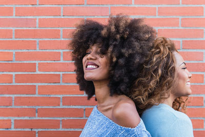 Side view smiling african american women with long afro hair and glamour makeup posing in brick wall